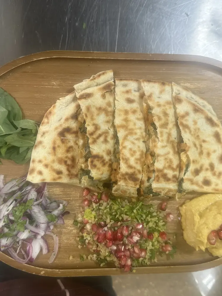 Sliced Turkish gözleme on a wooden board with red onion salad, bulgur, pomegranate and hummus