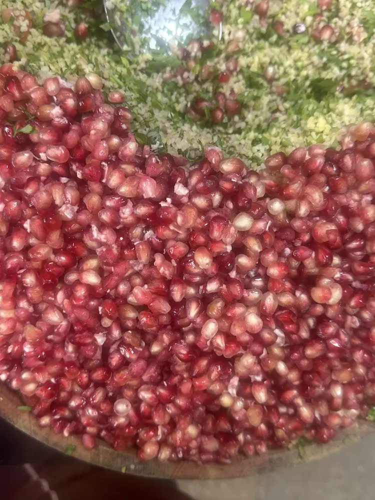 Large wooden bowl of pomegranate seeds over bulgur, parsley and herbs