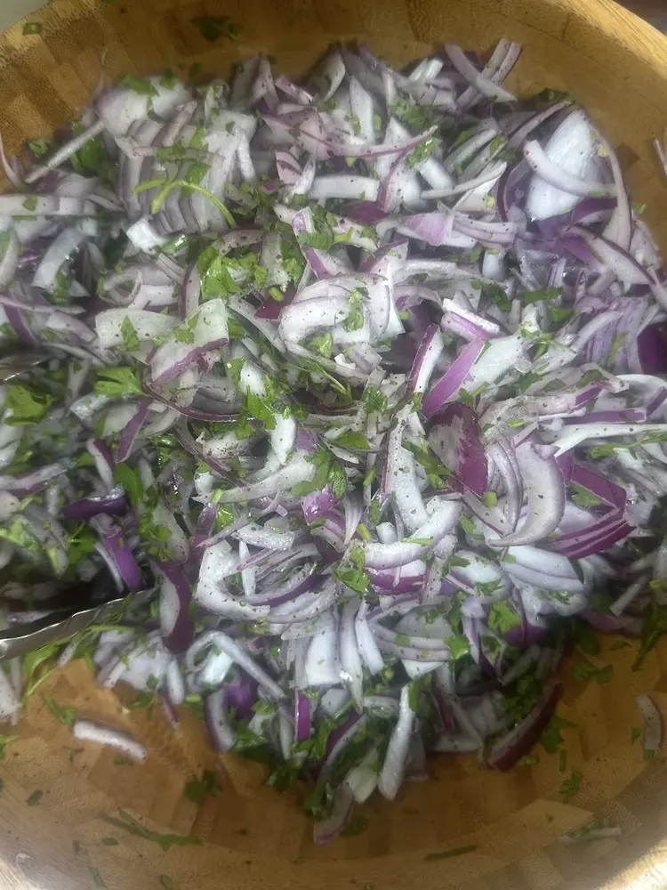Wooden bowl of sliced red onion with chopped parsley and sumac